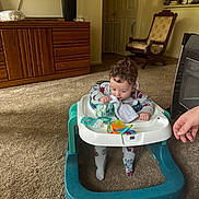 Emmett is registered to the contest to win money with this photo: toddler, walker, blanket, toy, carpet, living_room, wooden_cabinet, rocking_chair, television, foot, hand, curly_hair, pajamas, baby, indoor, person, furniture, carpeted_floor, child, family