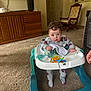 Emmett is registered to the contest to win money with this photo: baby, child, walker, curly_hair, pajamas, toy, blanket, carpet, living_room, rocking_chair, wooden_furniture, television, floor, hand, foot, person, indoor, cozy, expression, curious