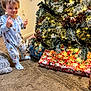 carpet, celebration, child, christmas_tree, cozy, decorations, family, festive, holiday, home, indoor, lights, pajamas, pine_cones, presents, smiling, toddler, winter, wrapped_gifts, young_child