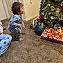 carpet, celebration, child, christmas_tree, crouching, decorations, door, festive, floor, gift_wrap, holiday, home, indoor, lights, pajamas, person, presents, socks, wall, young_child