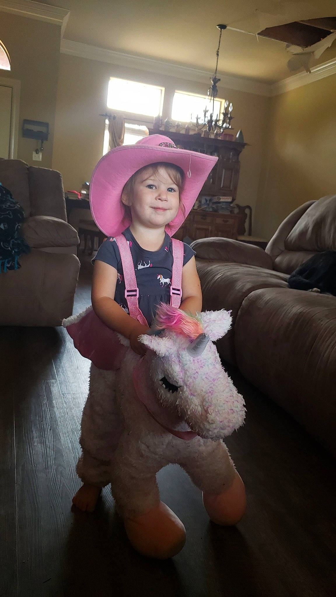 Elsa is registered to the contest to win money with this photo: baby_toddler_clothing, ceiling, couch, floor, flooring, hat, headwear, home_accessories, human, interior_design, joy, lamp, lampshade, light_fixture, living_room, person, pink, plush, room, stuffed_toy