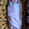 baby, infant, blanket, swaddle, smile, face, blue_eyes, happy, lying_down, patterned_blanket, sunflower, fabric, soft_texture, cozy, portrait, child, indoors, cute, wrapped, resting