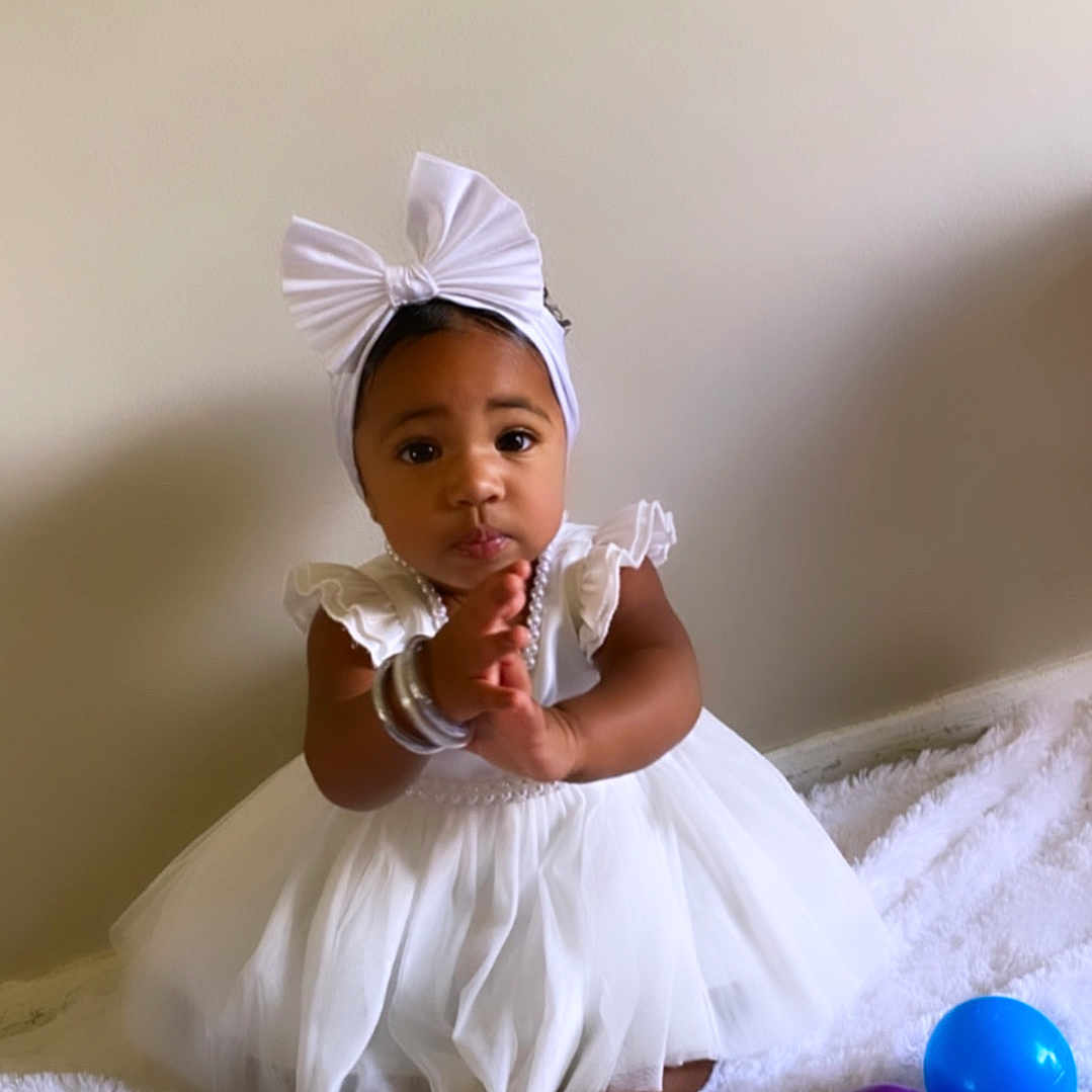 Yaneliz joined the competition — help win amazing prizes! baby, child, white_dress, bow_headband, clapping, sitting, blanket, indoor, toys, colorful_balls, purple_ball, blue_ball, cute, adorable, infant, soft_texture, happy, portrait, young_child, clothing