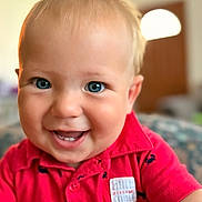 Jake is registered to the contest to win money with this photo: baby, toddler, child, smiling, blue_eyes, blond_hair, red_shirt, close_up, portrait, indoors, living_room, bokeh, lamp, teeth, cheeks, collar, skin, person, eyes, cute