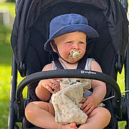 Soan a rejoint le concours — aidez-le/la à gagner de superbes lots ! baby, black_stroller, blanket, blue_hat, child, comfort, cute, foot, greenery, hand, legs, outdoor, pacifier, portrait, seatbelt, sitting, stroller, summer, sunlight, toddler