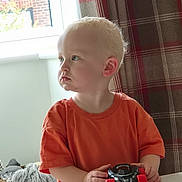 Carson joined the competition — help win amazing prizes! toddler, child, toy_car, orange_shirt, indoor, window, curtain, plaid, basket, blanket, table, person, young_child, light, portrait, focused, home, furniture, hand, cute