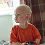 toddler, child, toy_car, orange_shirt, indoor, window, curtain, plaid, basket, blanket, table, person, young_child, light, portrait, focused, home, furniture, hand, cute