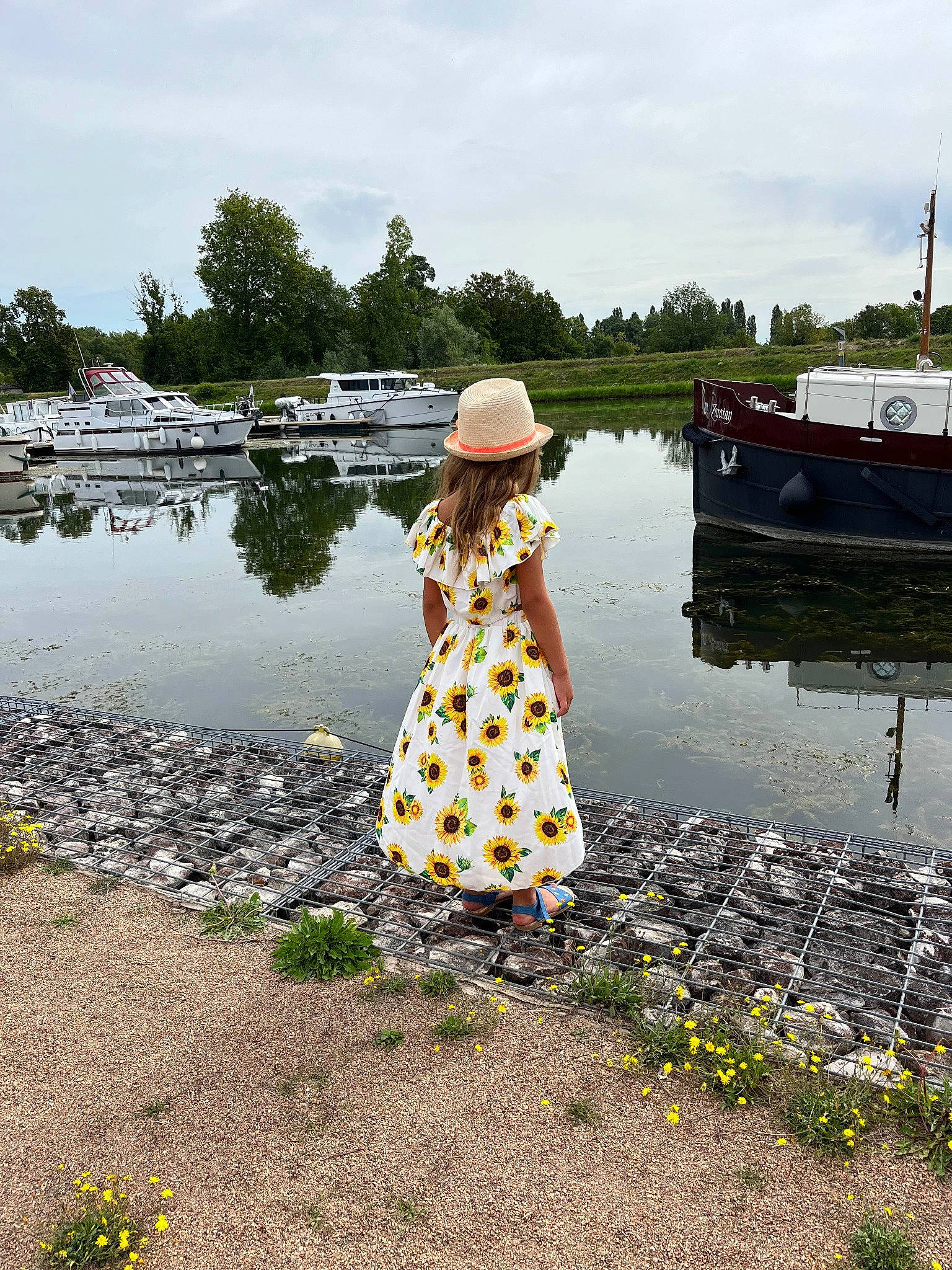 Emma participe au concours pour gagner de l'argent avec cette photo : bank, boat, boats_and_boating_equipment_and_supplies, body_of_water, cloud, flower, fun, grass, happy, hat, lake, leisure, morning, people_in_nature, person, plant, recreation, sky, sun_hat, tree