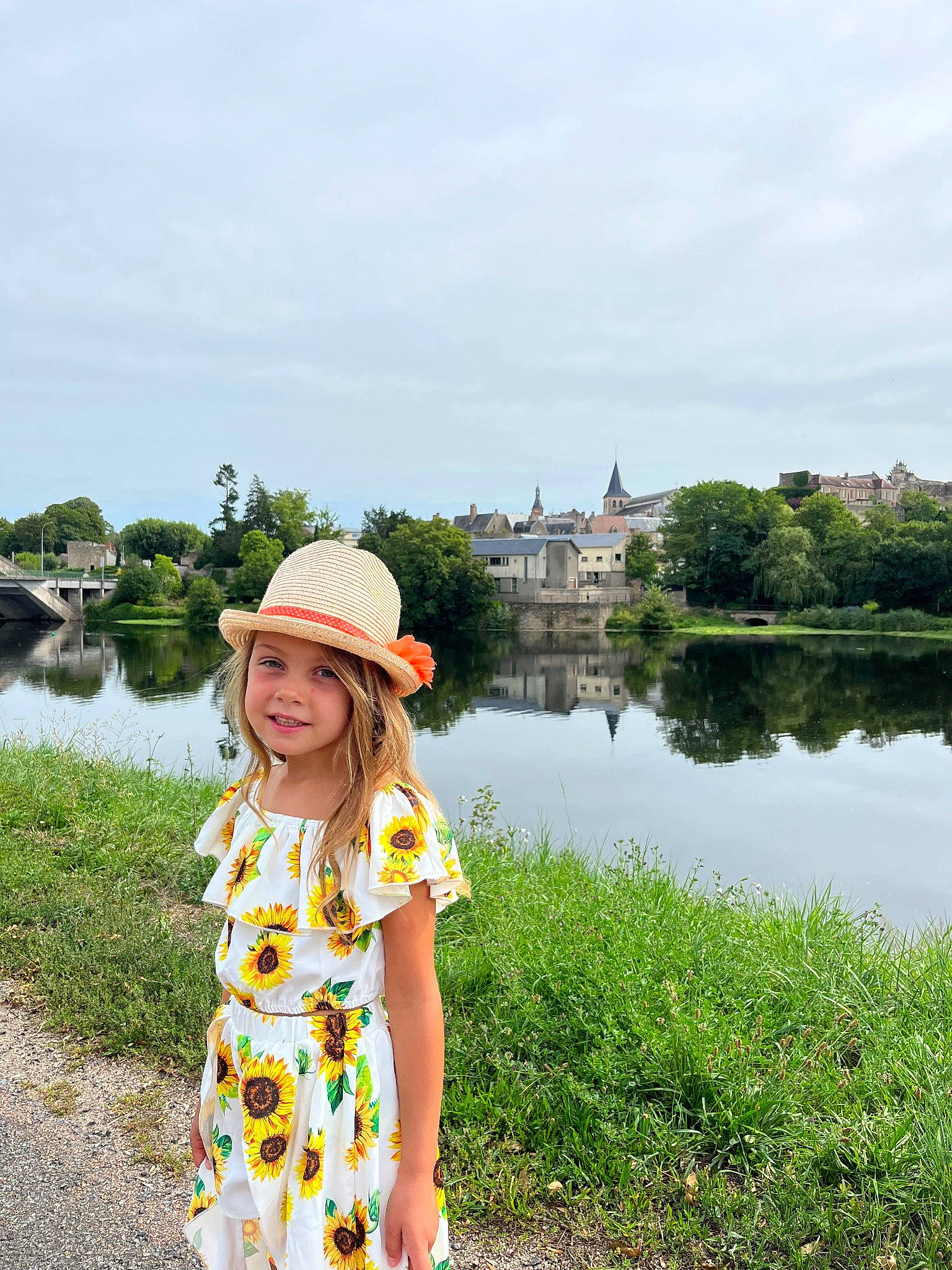 Emma a rejoint le concours — aidez-le/la à gagner de superbes lots ! bank, cloud, fun, grass, happy, hat, headwear, joy, lake, landscape, leisure, people_in_nature, person, plant, recreation, sky, smile, summer, sun_hat, toddler