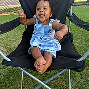 Davina is registered to the contest to win money with this photo: baby, child, smiling, blue_dress, striped, chair, outdoor, grass, happy, cute, sitting, black_chair, summer, sunny, portrait, infant, playful, person, curly_hair, barefoot