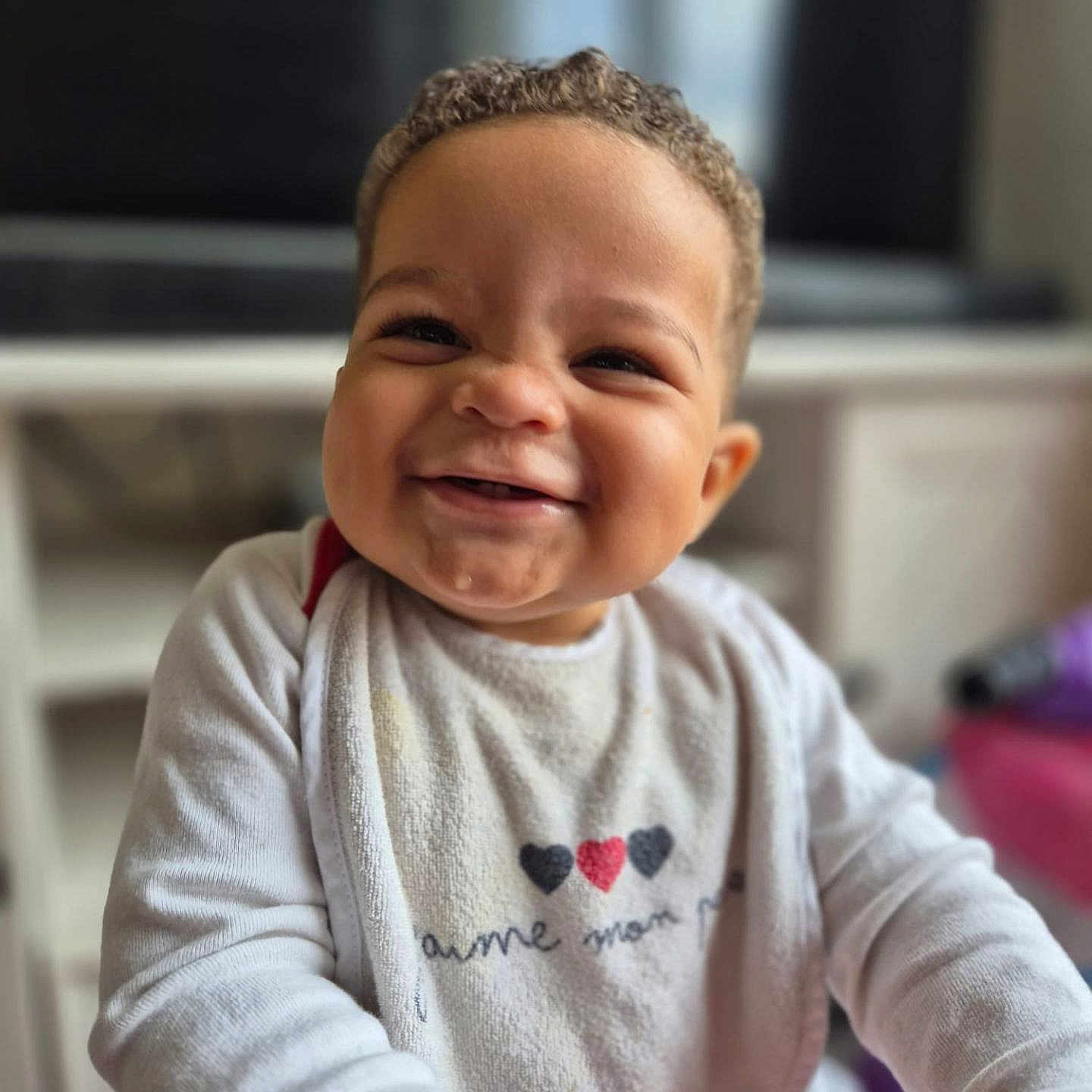 Zakarya participe au concours pour gagner de l'argent avec cette photo : baby, background, bib, child, closeup, curly_hair, cute, expression, face, furniture, happy, indoor, infant, person, portrait, sitting, skin, smiling, white_clothing, young_child