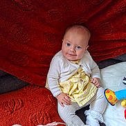 Gracie joined the competition — help win amazing prizes! baby, child, infant, smiling, sitting, yellow_dress, white_cardigan, white_socks, lace, pacifier, pacifier_clip, toy, blanket, red_blanket, soft_toy, blue_eyes, indoor, portrait, cute, cozy
