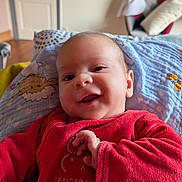 Antonin participe au concours pour gagner de l'argent avec cette photo : baby, smiling, red_clothing, blanket, indoor, infant, face, happy, cute, child, soft_toys, pattern, furniture, living_room, person, portrait, closeup, warm, comfort, home