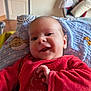 baby, smiling, red_clothing, blanket, indoor, infant, face, happy, cute, child, soft_toys, pattern, furniture, living_room, person, portrait, closeup, warm, comfort, home