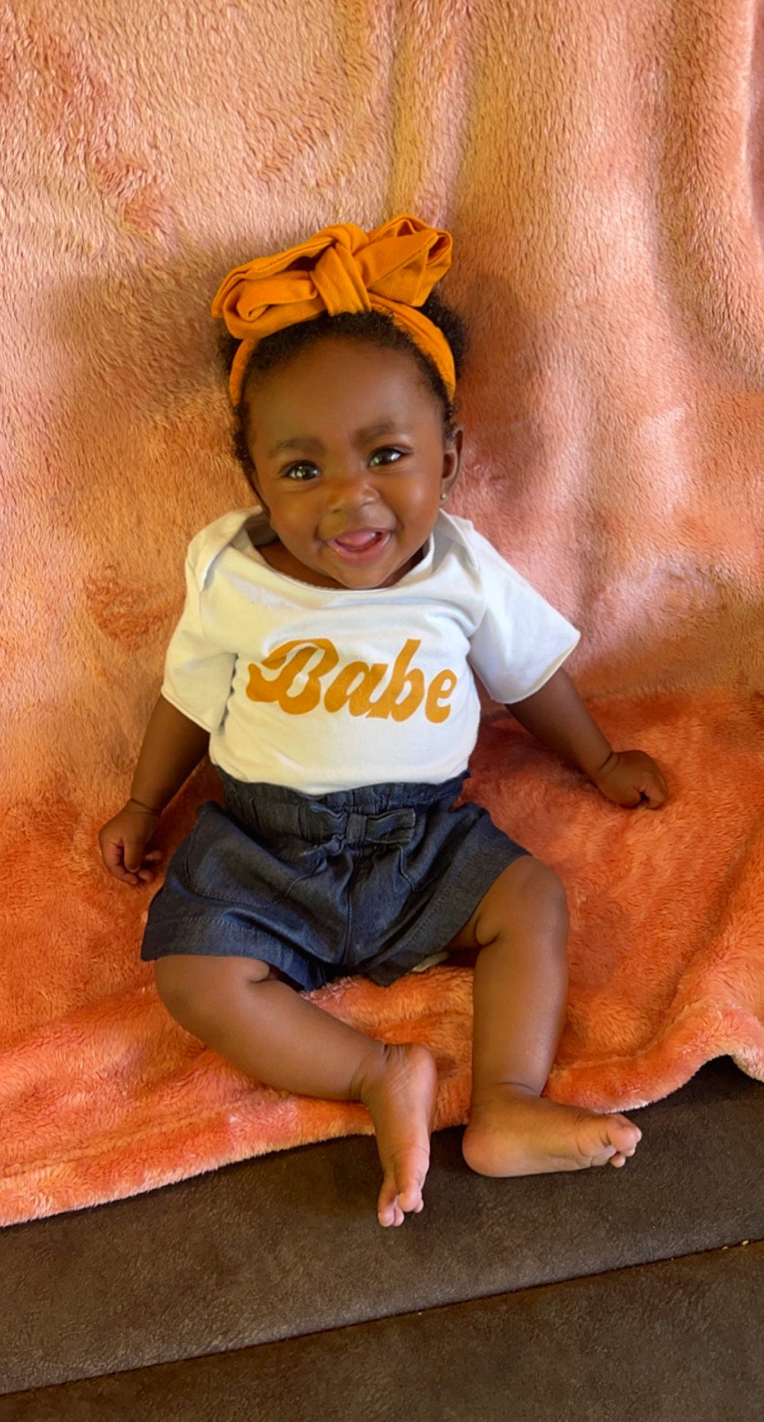 Lailah joined the competition — help win amazing prizes! baby, baby_toddler_clothing, barefoot, child, costume_hat, eye, fashion_accessory, flooring, foot, fun, happy, head, human_leg, joy, person, sitting, sleeve, smile, t_shirt, thigh