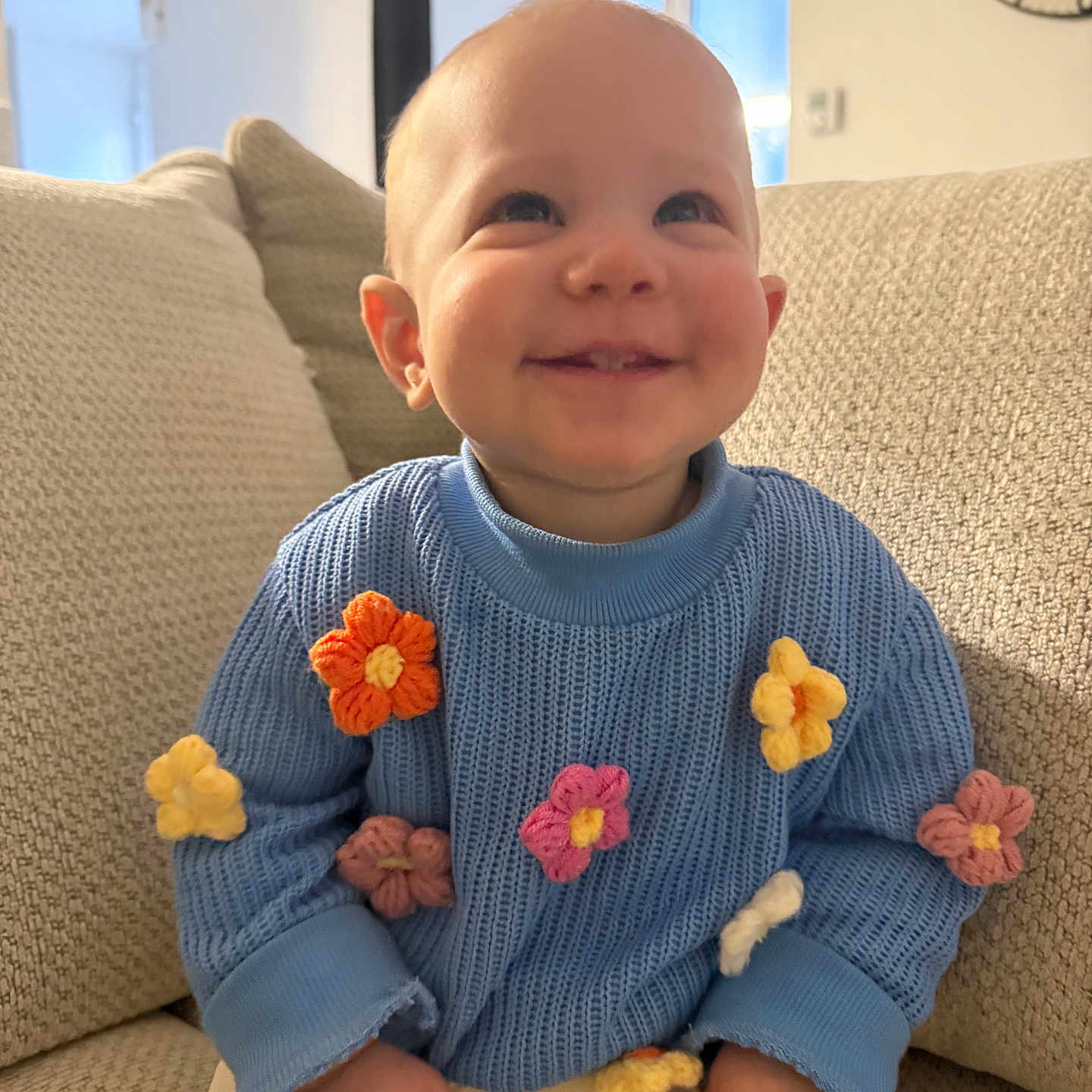 Leyana a rejoint le concours — aidez-le/la à gagner de superbes lots ! baby, blue_sweater, casual_clothing, cheerful, child, couch, cozy, cute, furniture, happy, home, indoor, infant, knitted_flowers, person, portrait, sitting, small_child, smiling, warm_light