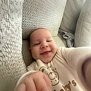 Leyana participe au concours pour gagner de l'argent avec cette photo : baby, smiling, infant, couch, fabric, onesie, clothing, hand, face, child, portrait, indoor, happy, person, cozy, texture, furniture, cute, playful, relaxed