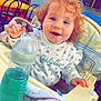 baby_bottle, blanket, blue_liquid, bottle, chair, child, clothing, curly_hair, curtain, face, happy, high_chair, indoor, person, playground, red_hair, smile, soft_toy, table, toddler