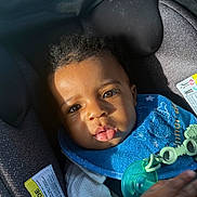 Wisdom is registered to the contest to win money with this photo: baby, child, car_seat, blue_bib, pacifier, sunlight, face, eyes, hair, clothing, infant, seat_belt, closeup, portrait, expression, cute, indoors, hand, skin, young