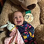 baby, smile, teddy_bear, stuffed_animal, blanket, bunny, infant, clothing, floral_pattern, face, happy, child, portrait, cute, soft_toy, milestone, indoor, baby_girl, cuddly, comfort