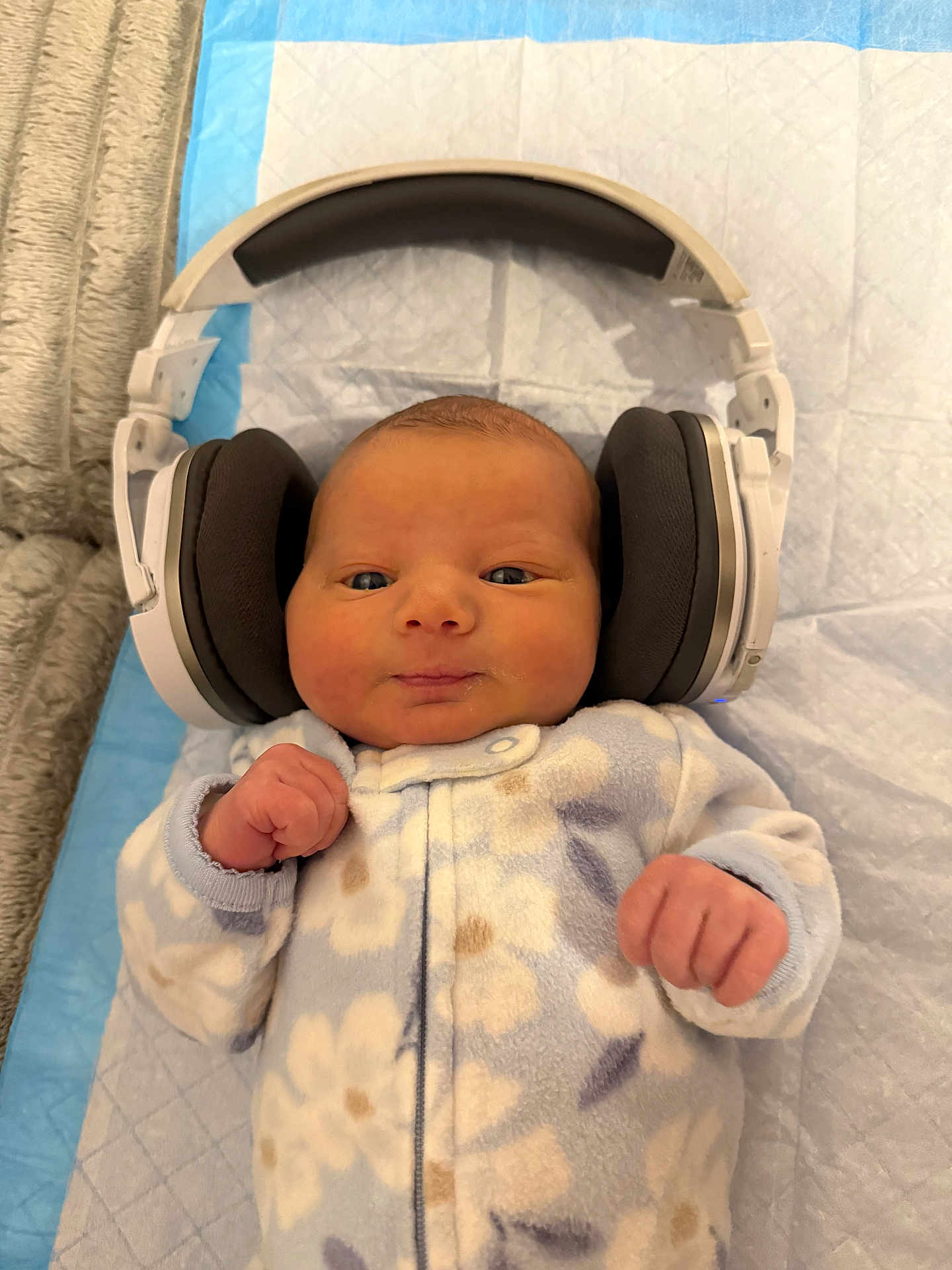 Lorelei is registered to the contest to win money with this photo: baby, newborn, infant, headphones, oversized_headphones, onesie, floral_onesie, lying_down, changing_pad, blanket, face, hands, cute, portrait, indoors, nursery, soft_texture, earpads, cozy, photography