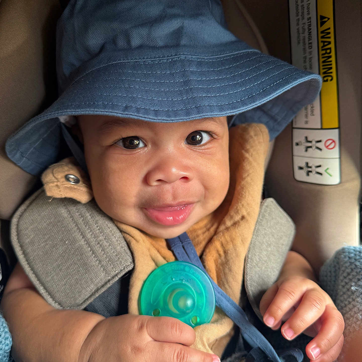 Tamari is registered to the contest to win money with this photo: baby, blanket, blue_hat, car_seat, child, clothing, cute, eyes, face, hand, headwear, indoors, infant, pacifier, person, portrait, seatbelt, skin, smile, young_child