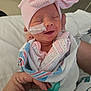 newborn, baby, hospital, blanket, pacifier, hat, pink, bow, smile, sleeping, hand, nail_polish, person, infant, medical_tape, clothing, wrapped, cute, indoors, patient