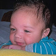Ali is registered to the contest to win money with this photo: baby, child, face, smile, blue_striped_clothing, indoor, closeup, resting, cute, infant, skin, hand, head, eyelashes, cheeks, person, portrait, happy, soft_light, cozy