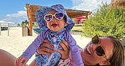 Poppy is registered to the contest to win money with this photo: baby, woman, sunglasses, hat, beach, sand, sunny, smile, joyful, outdoor, ocean, vacation, summer, happy, child, parent, sunhat, colorful_clothing, nature, relaxation