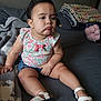 child, toddler, baby, indoor, bed, blanket, plush_toy, clothing, footwear, pout, sitting, person, cute, expression, home, casual, comfort, soft_lighting, shorts, floral