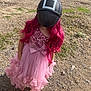 child, pink_dress, wig, helmet, barefoot, outdoor, dirt_path, rocks, grass, sequins, bow, long_hair, costume, playful, fashion, young_person, standing, nature, funny, disguise