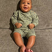 Javonte is registered to the contest to win money with this photo: baby, child, smiling, sitting, couch, sofa, indoors, clothing, dinosaur_print, happy, infant, person, foot, legs, face, cute, young, casual_wear, home, comfort