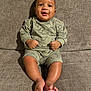 baby, child, smiling, sitting, couch, sofa, indoors, clothing, dinosaur_print, happy, infant, person, foot, legs, face, cute, young, casual_wear, home, comfort