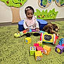 baby, child, toy, colorful, blocks, plush_toy, carpet, indoor, playroom, smiling, girl, headband, caterpillar_toy, decor, wall_art, green, floor, seated, clothing, play