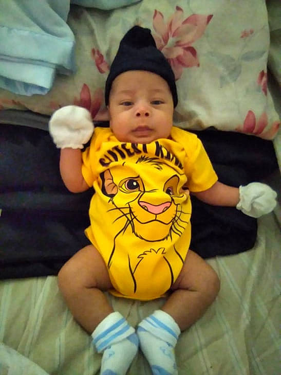 Jenesis is registered to the contest to win money with this photo: abdomen, baby, baby_toddler_clothing, cheek, child, comfort, eye, finger, gesture, happy, head, headwear, person, product, skin, sleeve, t_shirt, textile, thigh, thumb