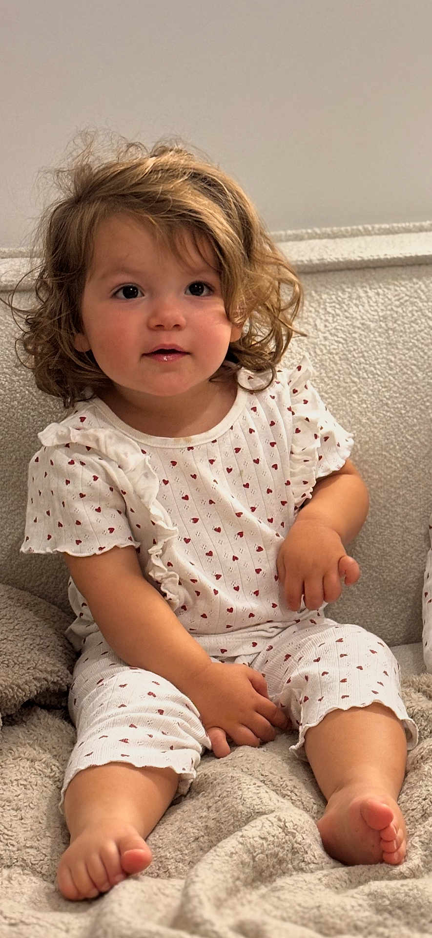 Alba a rejoint le concours — aidez-le/la à gagner de superbes lots ! toddler, child, curly_hair, white_outfit, hearts_pattern, sitting, blanket, cozy, indoors, soft_lighting, barefoot, cute, portrait, face, young_child, comfortable, clothing, relaxed, close_up, baby