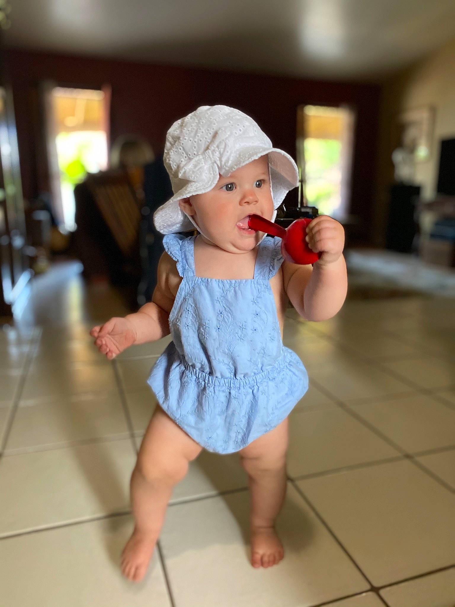Finley is registered to the contest to win money with this photo: baby, baby_toddler_clothing, baseball_cap, cap, dress, floor, flooring, foot, happy, hat, headwear, human_leg, leisure, one_piece_garment, person, shoe, sleeve, sun_hat, surprise, thigh