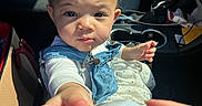 Reya joined the competition — help win amazing prizes! child, toddler, red_bow, denim_overalls, white_shirt, car_interior, car_seat, cup_holder, hand, face, curious, infant, seatbelt, sunlight, window_light, baby, person, close_up, expression, reaching