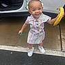 toddler, child, smiling, banana, pastel_dress, white_sneakers, hair_bows, car, open_door, pavement, outdoor, happy, playful, pacifier, rain_drops, concrete, person, cute, standing, daylight