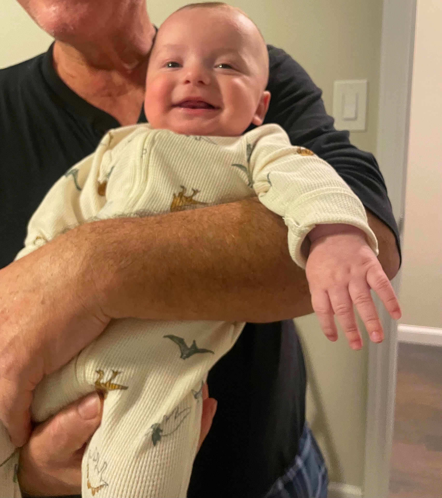 Leonardo is registered to the contest to win money with this photo: adult, arm, baby, casual, child, clothing, dinosaur_pattern, doorway, face, hand, happy, holding, home, indoor, light_switch, onesie, person, portrait, skin, smiling