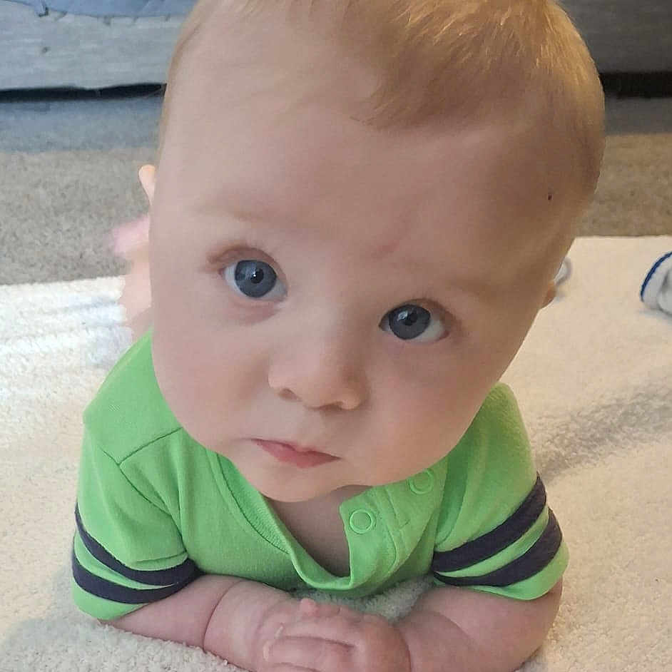 Karter joined the competition — help win amazing prizes! baby, baby_pose, blue_eyes, carpet, child, closeup, cute, expression, face, floor, green_shirt, hair, hands_clasped, indoor, infant, person, portrait, skin, towel, young