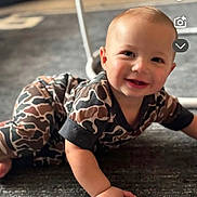 Aiden is registered to the contest to win money with this photo: baby, crawling, carpet, indoor, smiling, child, pajamas, camo_pattern, face, young_child, cute, happy, person, floor, head, skin, hand, photography, infant, social_media