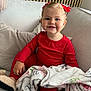 toddler, child, red_pajamas, blanket, couch, smile, happy, curly_hair, bow, slippers, indoor, cozy, soft_texture, person, portrait, seated, home, comfort, furniture, cute