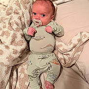 Kayce joined the competition — help win amazing prizes! baby, infant, pacifier, pajamas, dinosaur_print, blanket, bed, cozy, soft_texture, cute, sleepwear, foot, hand, face, expression, indoors, sleeping_area, comfort, child, newborn