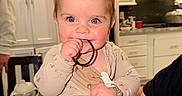 Kayce joined the competition — help win amazing prizes! baby, child, kitchen, onesie, hair_tie, chewing, curious_eyes, cute, indoor, modern_kitchen, white_cabinets, stove_hood, person, infant, playing, seated, pacifier_clip, toy, smiling, hand