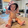 Kayce is registered to the contest to win money with this photo: baby, child, diaper, hat, kitchen, countertop, food_crumbs, smiling, happy, sitting, indoors, person, cute, cheerful, face, hand, foot, window, cabinet, appliance