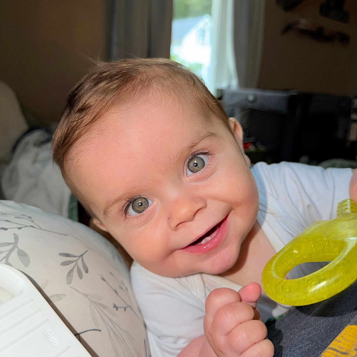 Kayce is registered to the contest to win money with this photo: baby, child, smiling, teething_ring, hand, face, eyes, indoors, window, curtains, furniture, white_clothing, skin, cheeks, light, portrait, candid, cute, happy, infant