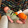 baby, pacifier, plush_toy, pumpkin, armchair, blanket, halloween, text_pattern, infant, cute, smiling, cozy, indoor, person, child, soft_toy, holiday, celebration, relaxing, casual