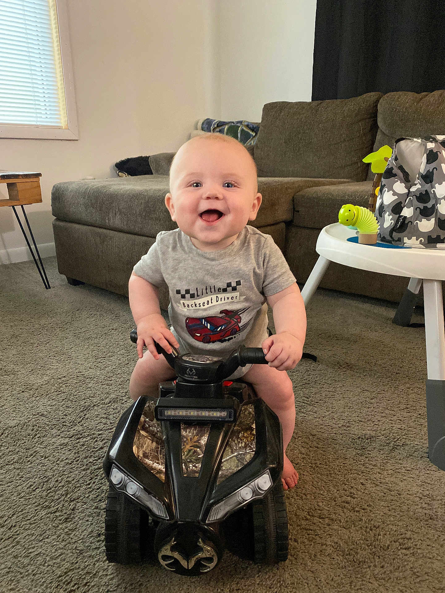 Ryder joined the competition — help win amazing prizes! baby, child, smiling, toy_vehicle, indoor, carpet, living_room, sofa, table, window, curtain, toy, happy, person, crawling_toy, car, cute, playful, infant, furniture