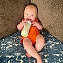 Ryder joined the competition — help win amazing prizes! baby, infant, bottle, milk, orange_onesie, blue_eyes, cushion, blanket, patterned_blanket, happy, smiling, sitting, indoors, child, cute, milk_bottle, soft_furniture, comfort, cozy, portrait